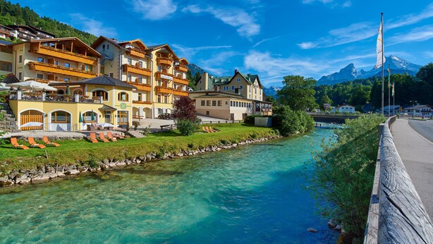 Un hotel con varios balcones, un río y una montaña al fondo.