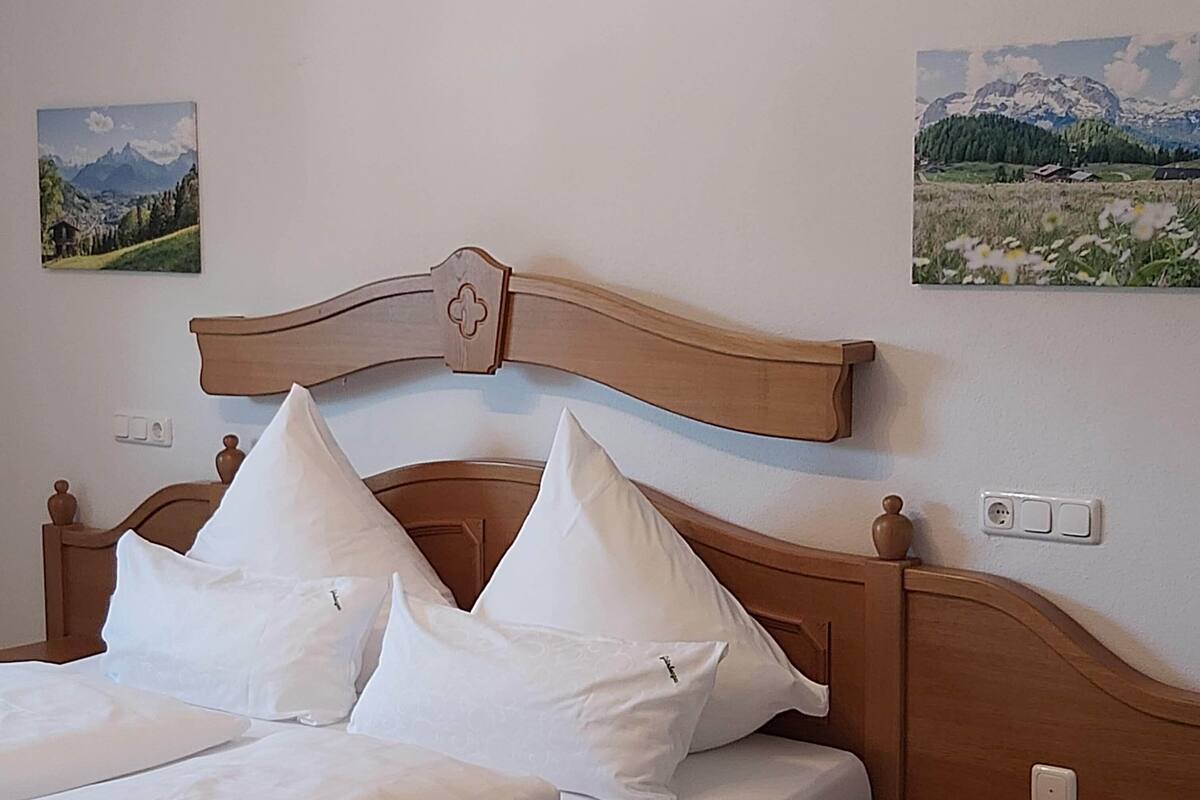 Cama com roupa de cama e almofadas brancas, cabeceira de madeira e duas mesas de cabeceira.