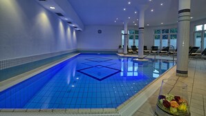 Una piscina interior con paredes y techo azulejados, sillas de descanso y un reloj en la pared.