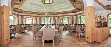 A spacious dining area with wooden beams, large windows, and a central chandelier.