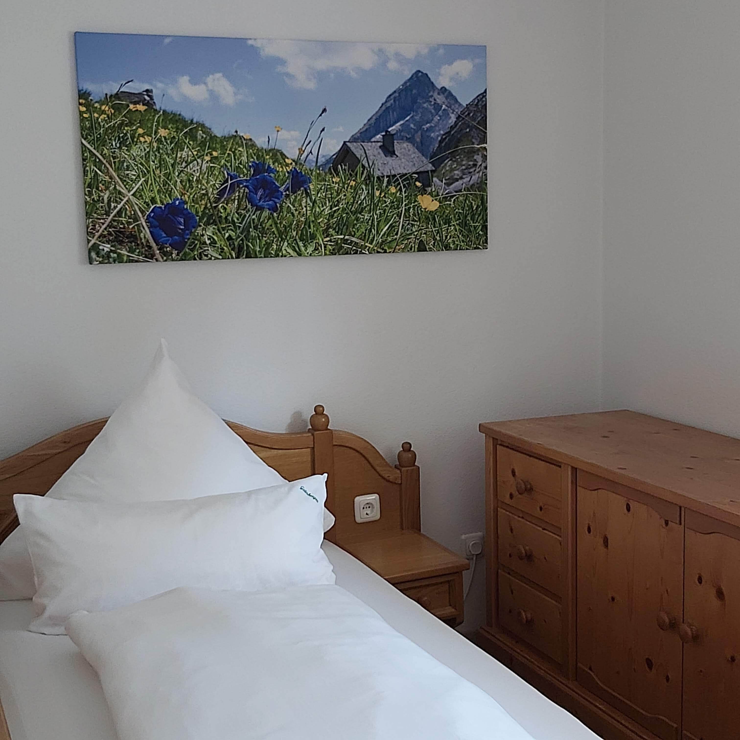 Un dormitorio con una cama, una mesita de noche de madera, un aparador de madera y un cuadro de un paisaje montañoso.