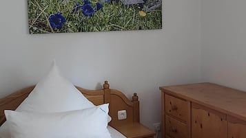 Une chambre à coucher comprenant un lit, une table de chevet en bois, une commode en bois et un tableau représentant un paysage de montagne.