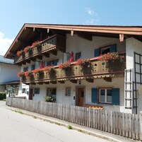 Una cabaña tradicional con varios balcones decorados con flores rojas, barandillas de madera y una valla de madera al frente.