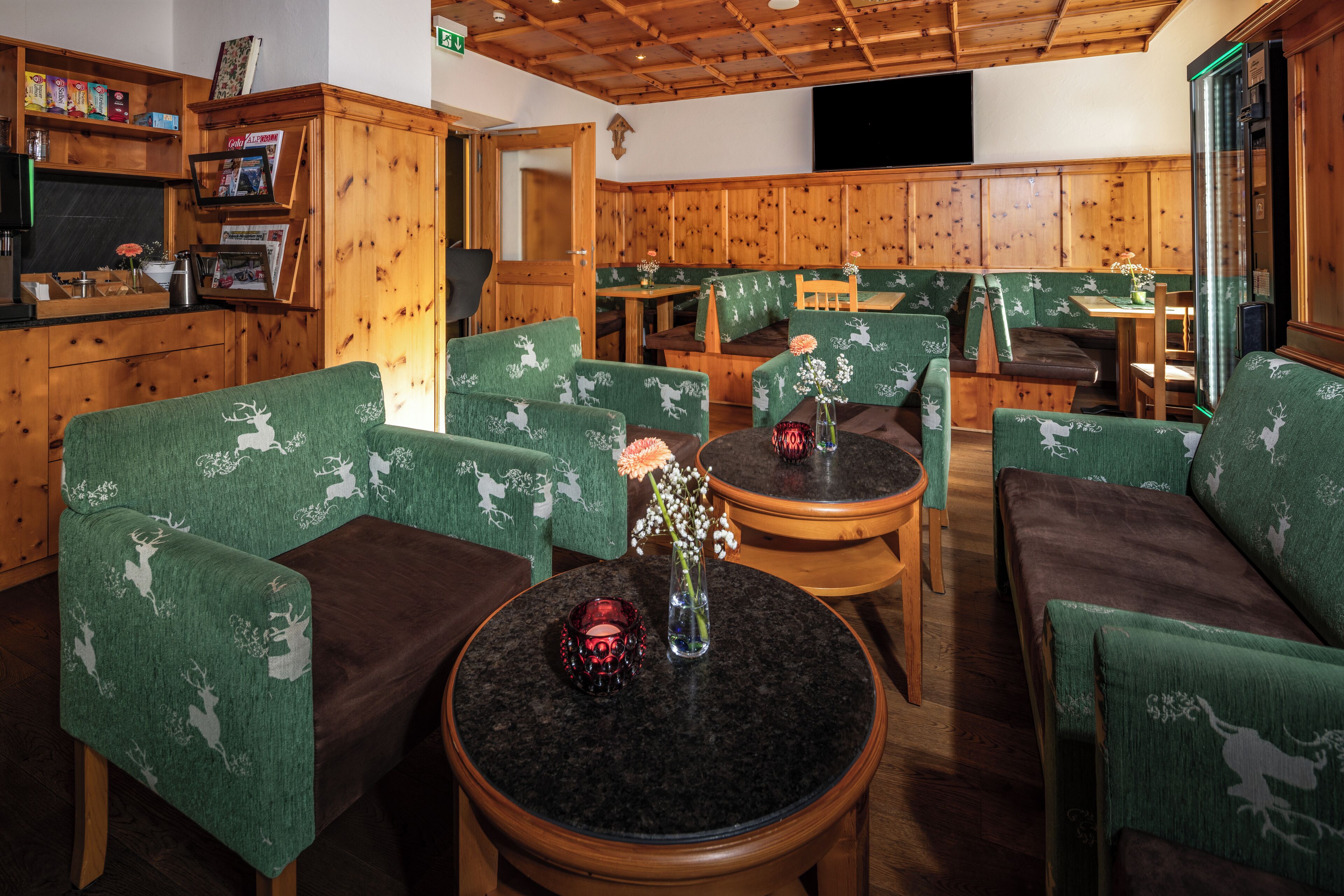 Un interior acogedor con paneles de madera, sillas tapizadas en verde y una pequeña mesa con un florero.