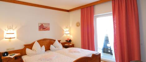 A bedroom with a wooden bed, two bedside lamps, a nightstand, a window with curtains, and a view of a building outside.