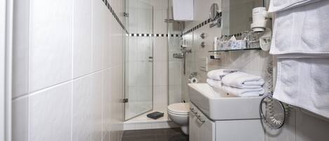 Un baño moderno con cabina de ducha de vidrio, un lavabo blanco con toallero y un inodoro.