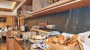 Montaje de bufé con diversos alimentos, como pan, pasteles y salsas, dispuesto en una barra de madera con salpicadero de mármol.