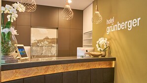 Zona de recepción de un hotel con diseño moderno, que incluye un mostrador, iluminación decorativa y un cartel en la pared.