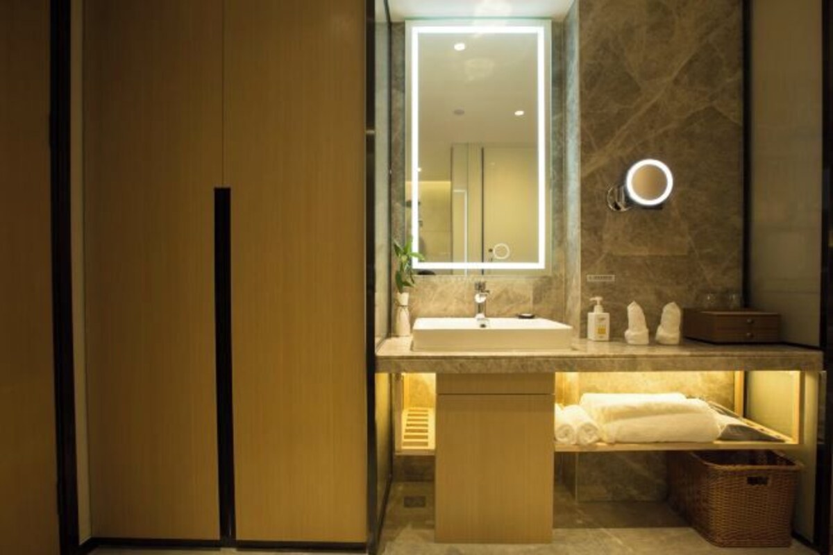 A modern bathroom with a wooden vanity, a mirror with built-in lighting, a sink, and neatly arranged towels.