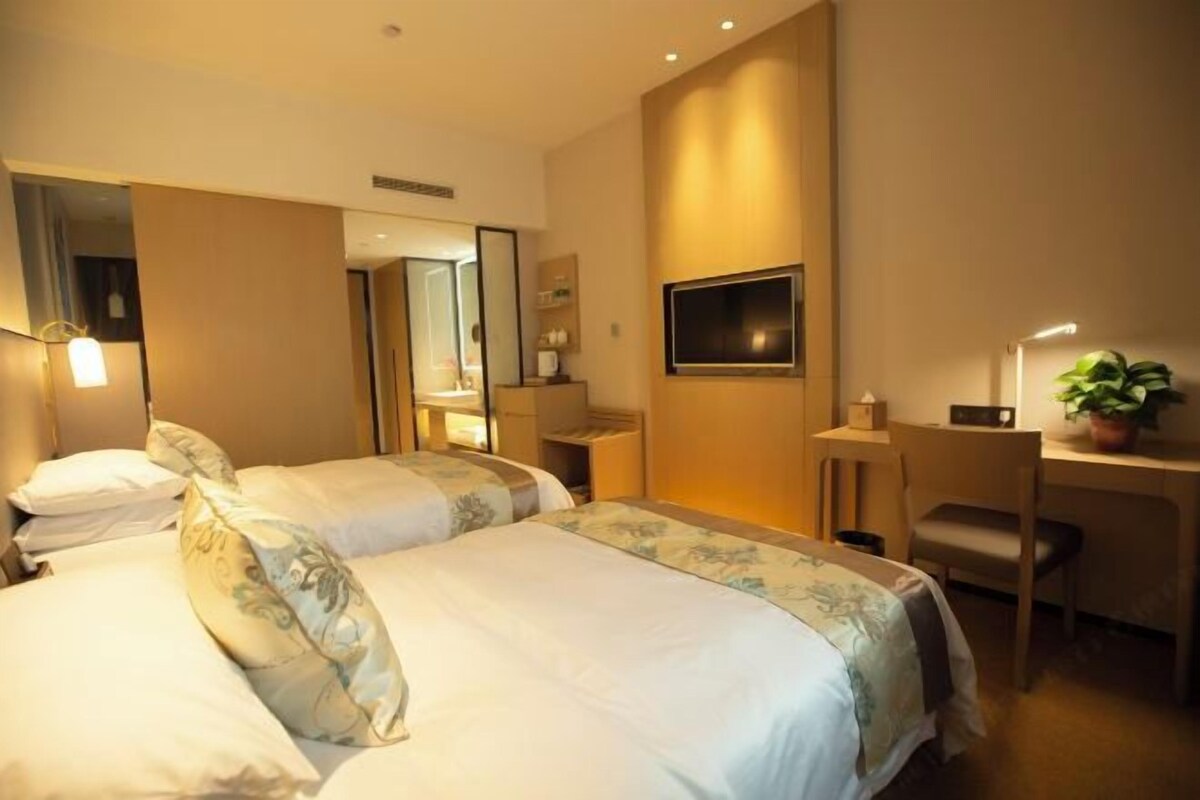 A hotel room with two beds, a desk, a chair, a TV, and a potted plant.