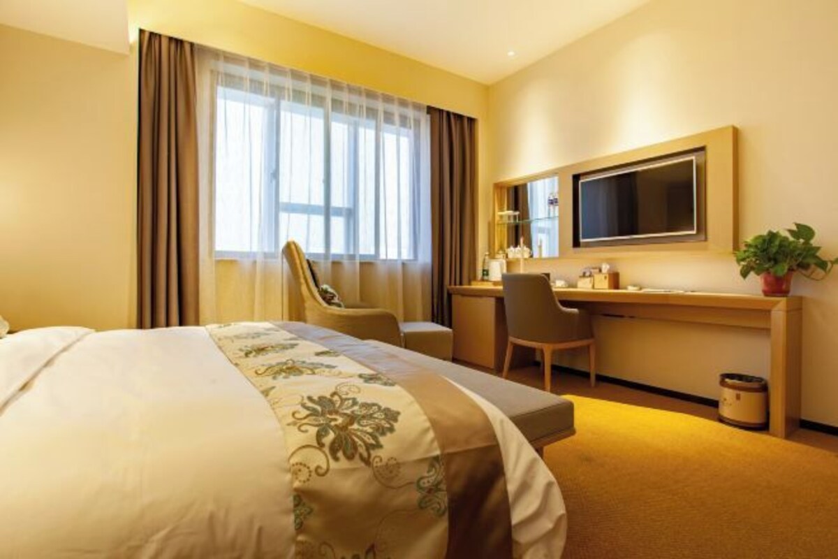 A hotel room with a bed, a desk, a chair, a TV, and a plant.