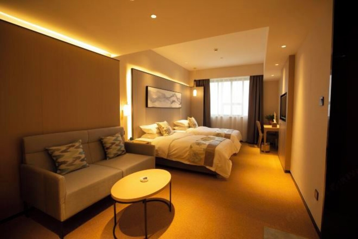 A hotel room with a bed, a sofa, a small round table, and a TV.