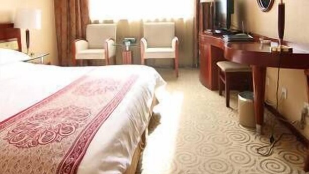 Una habitación de hotel con una cama grande, dos sillones, un escritorio con ordenador y un televisor.
