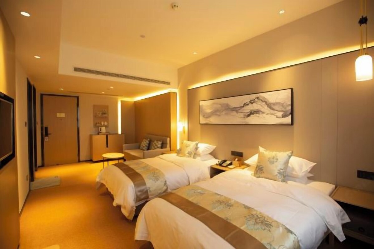A hotel room with two beds, a desk, a chair, and a painting on the wall.