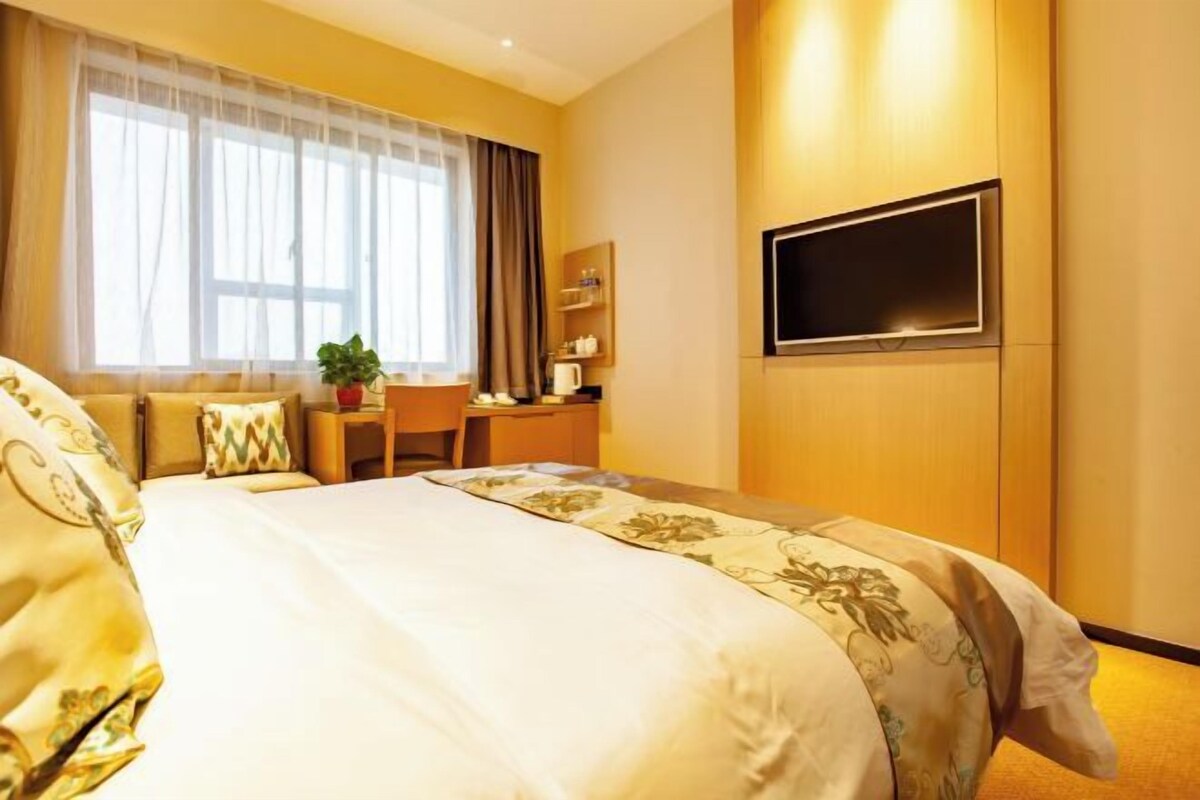 Una habitación de hotel con una cama grande, un escritorio, una silla, un televisor y un ventanal con cortinas.