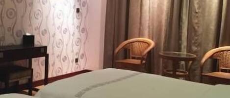 A hotel room with two beds, a desk, and two wicker chairs.