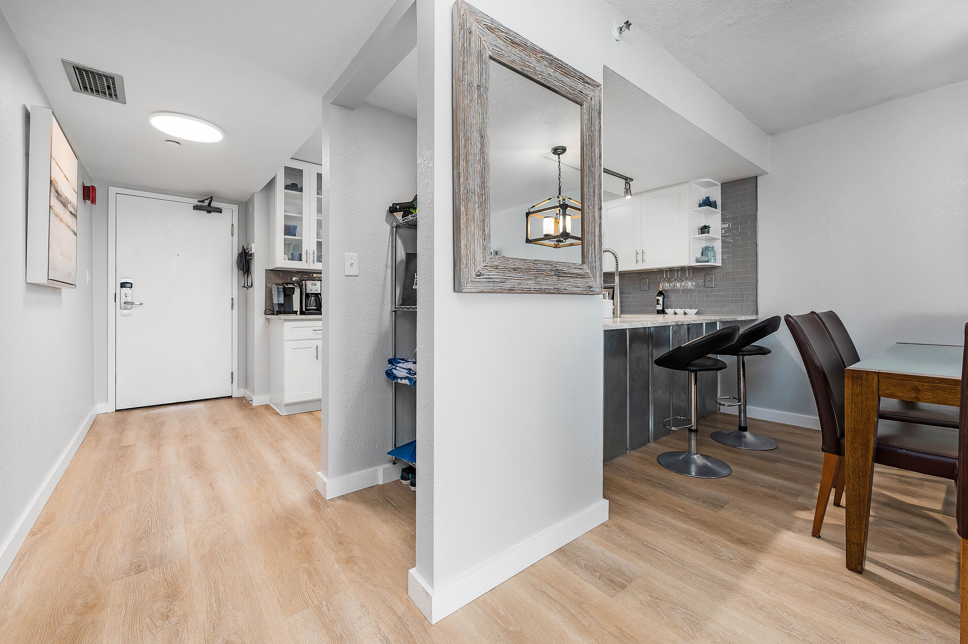 A modern kitchen with white cabinets, a dining area with a wooden table and black chairs, and a large mirror on the wall.