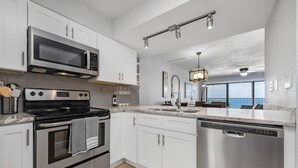 A modern kitchen with stainless steel appliances, white cabinetry, and a large window providing a view. - BEACHFRONT-9th floor view, recently updated-avail Sept 7-12, 19-23, Oct 18-25 (Destin)