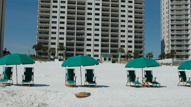 A beach with multiple green umbrellas and lounge chairs, a large hotel building in the background, and clear blue skies. - BEACHFRONT-9th floor view, recently updated-avail Sept 7-12, 19-23, Oct 18-25 (Destin)
