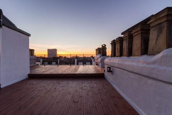 A rooftop terrace with a wooden deck, a view of the city skyline, and classical architectural columns. - 2 Palace Gardens (London)
