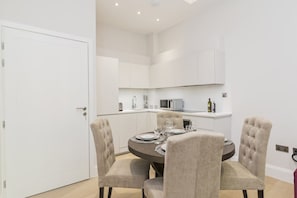 A modern kitchen with white cabinets, a microwave, and a dining area with a round table and four upholstered chairs.
