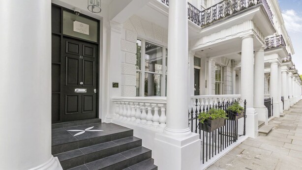 A building with white columns, a black door, and a staircase leading to a balcony with flower boxes. - 3b Imperial (London)