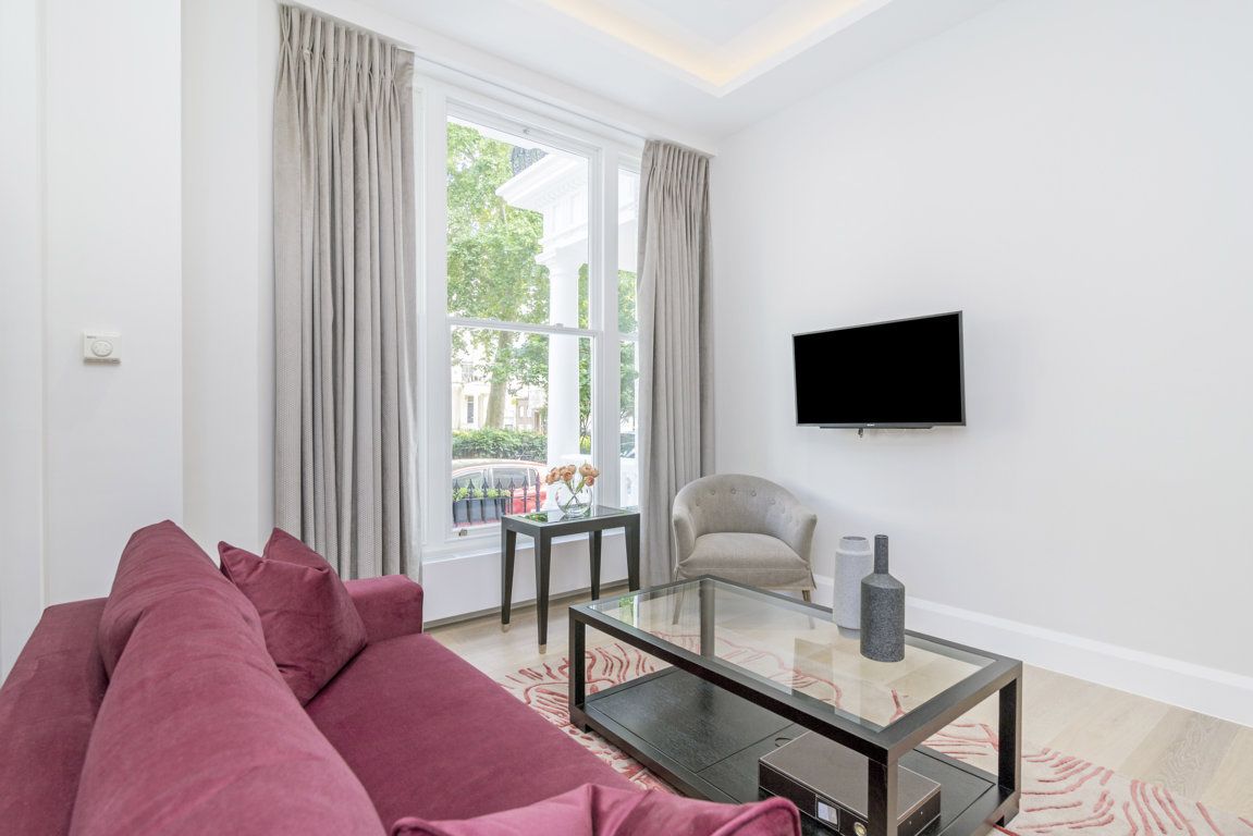 Un salon moderne avec une table basse en verre, un canapé rouge, un fauteuil beige et un téléviseur à écran plat fixé au mur.