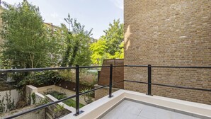 A rooftop terrace with a brick wall, a metal railing, and a view of a garden and trees. - 3b Imperial (London)