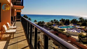 A balcony with a view of the ocean and a pool area with umbrellas.