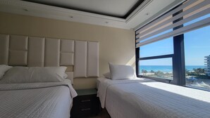 A hotel room with two beds, a large window with a view of the beach, and a modern ceiling design.
