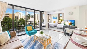 Un salon moderne comprenant un canapé, un fauteuil, une table basse, un téléviseur, une table à manger et un balcon offrant une vue sur la ville.
