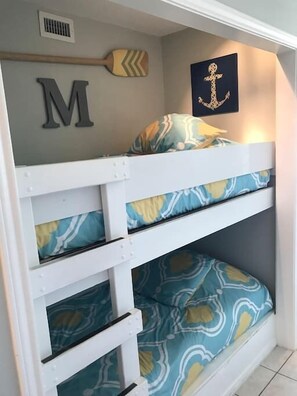 A bunk bed with patterned bedding, a wall-mounted letter 'M', a wall-mounted anchor, and a wooden paddle.