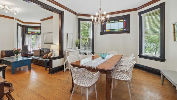 Un coin repas avec une table en bois, des chaises blanches et un lustre. Le salon adjacent est équipé d’un canapé et d’un téléviseur.