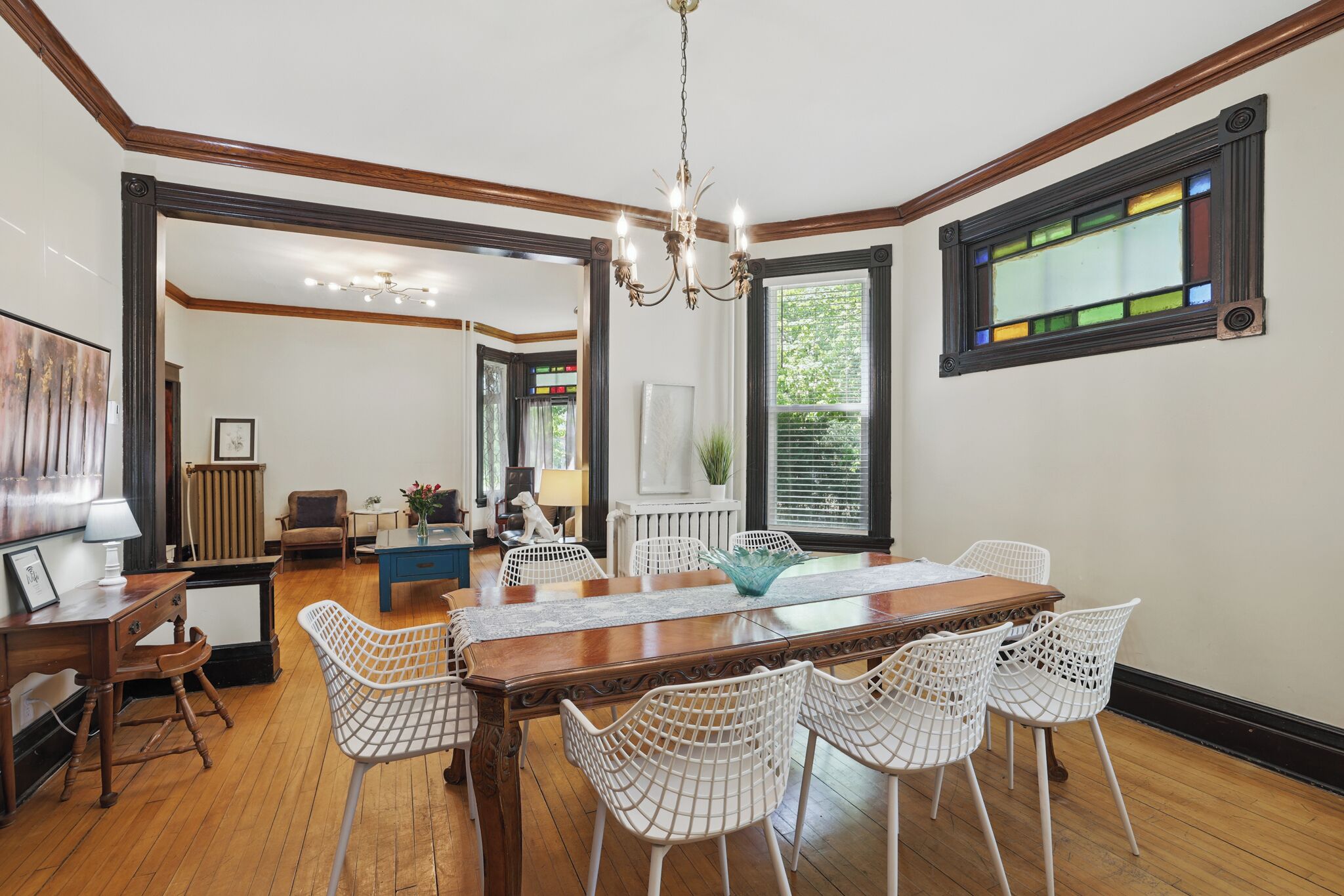 Un coin repas avec une table en bois et des chaises en fil de fer blanc, un lustre et une fenêtre à vitraux.