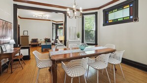 Un coin repas avec une table en bois et des chaises en fil de fer blanc, un lustre et une fenêtre à vitraux.