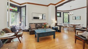 Un salon spacieux doté d’un parquet, d’une table basse bleue, d’un canapé en cuir marron et d’un coin repas avec des chaises blanches et une table en bois.