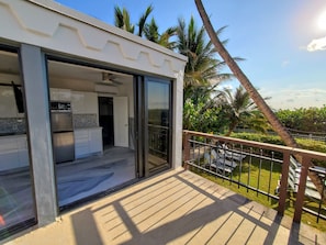 A modern kitchen with white cabinets and a stainless steel refrigerator, a sliding glass door leading to a balcony with a view of palm trees and a clear sky. - Large Deluxe Corner Apartment for Large Groups - 521 (Miami Beach)