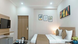 A hotel room with a bed, bedside table, TV, and a small kitchenette. - STEPiNN - Ess Kay Ess Villa (Gurugram)