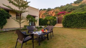 A patio with a table and chairs, surrounded by greenery and a building. - STEPiNN - Ess Kay Ess Villa (Gurugram)
