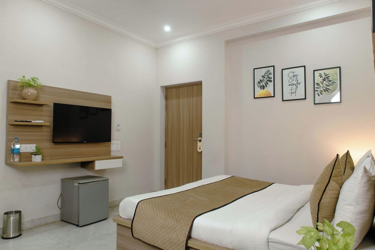 A hotel room with a bed, a TV mounted on the wall, a small fridge, and a door.