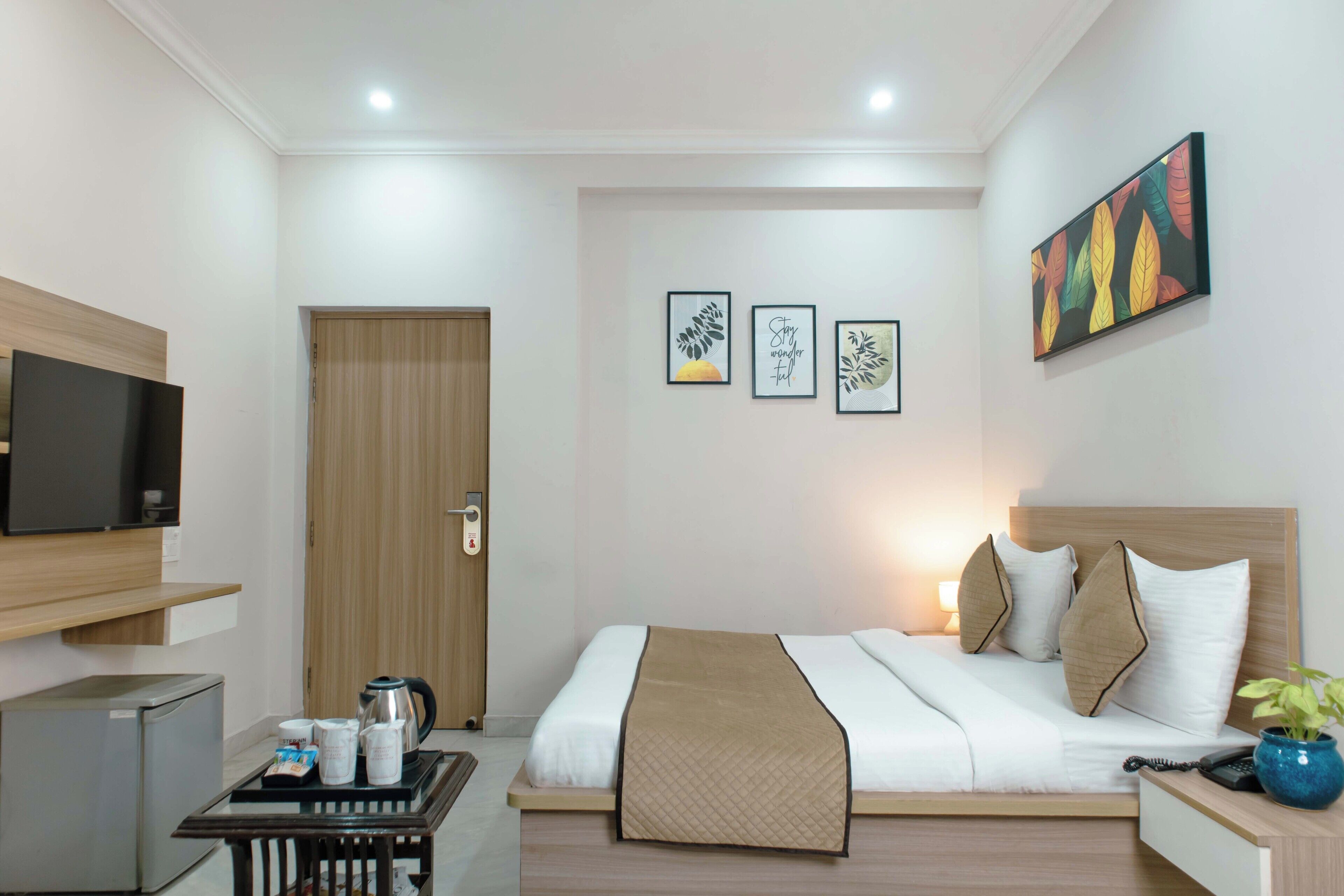 A hotel room with a bed, bedside table, TV, and artwork on the wall.