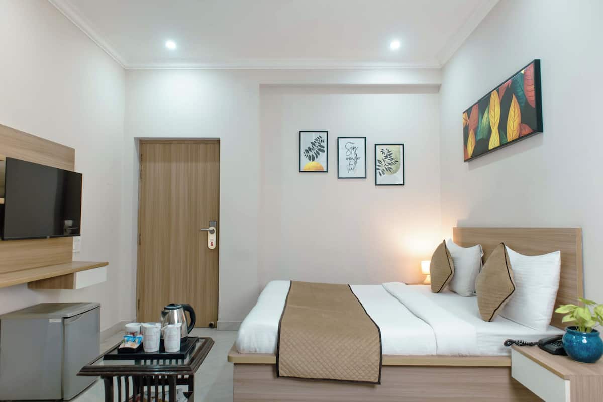 A hotel room with a bed, bedside table, TV, and artwork on the wall.