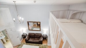 A bedroom with a bunk bed, a brown leather sofa, a white coffee table, a mirror, and a chandelier. - QB 11 (London)
