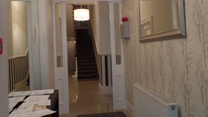 A hallway with a staircase, a radiator, a mirror, and a desk with papers. - QB 11 (London)