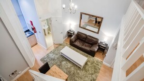 A modern living room with a brown leather sofa, a white coffee table, and a chandelier. - QB 11 (London)