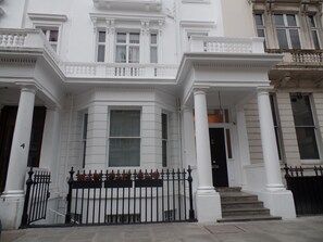 A white building with a classical architectural style, featuring a prominent entrance with steps and a black iron gate. - QB 6 (London)