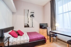 A bedroom with a bed, a desk, a TV, and a window with curtains. - QB 6 (London)