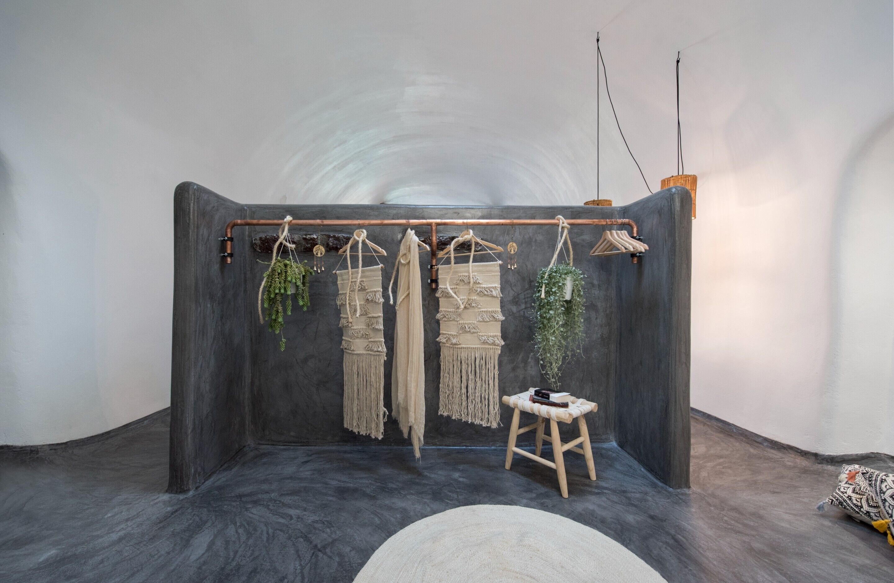 A room with a dark, curved wall, a macrame wall hanging, a small wooden stool, and a hanging plant.