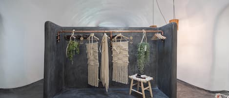 A room with a dark, curved wall, a macrame wall hanging, a small wooden stool, and a hanging plant.