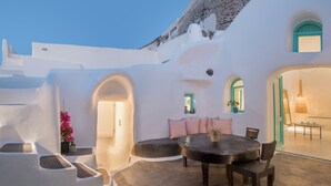 A white-walled building with a round table and chairs, a small window, and a door. - Sophia Finikia Villas (Santorini)